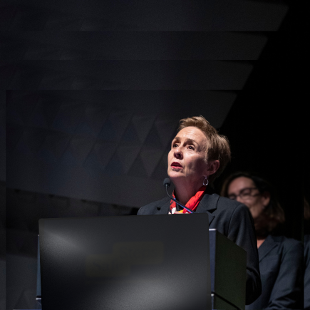 Commissioner Micaela Cronin making a public speaking appearance against a dark backdrop